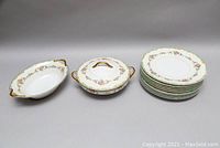 Full set of Noritake dinner plates stacked, lidded vegetable bowl, and oval serving bowl arranged on table.