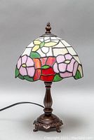 Photo of the front view of the stained glass table lamp showing floral patterns in the shade and metal base.