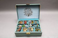 Open Lady Buxton jewelry box showing the tray with brooches, earrings, and rings including a red maple leaf brooch and a beaded heart brooch.