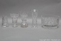 Front view of four cut crystal bud vases and one footed crystal fruit bowl arranged side by side on a surface, showing clear detailed cutting and different sizes.