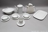 Full view of entire porcelain serving set showing lidded teapot, lidded serving bowl, rectangular platter, soup bowls with saucers, and mug with saucer.