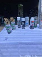 Full lot displayed including various spray paint cans with metallic gold caps, white primer, and rust protection sprays on a white surface.
