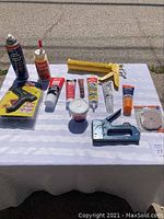 Full view of lot laid out on a table showing adhesives and tools including glue gun, caulk gun, staple gun, tubes and can of adhesive