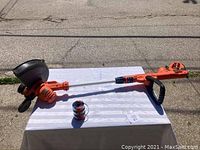 Black & Decker electric weed whacker laid on a table outdoors with a pack of replacement feed spindles also visible.