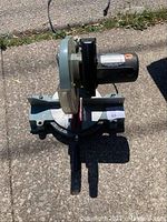 Full view of the Delta mitre saw showing motor, blade cover, handle and base on concrete surface outdoors.