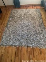 Full view of a rectangular shag leather rug laid on hardwood floor showing overall size and texture.