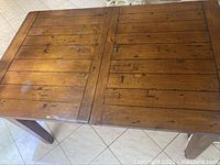 Top view of wooden dining table showing rectangular surface with visible grain and knots; center leaf seam visible where leaf folds inside.