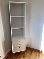 Front view of the white office shelf and drawer cabinet showing three shelves and two drawers with crystal pulls, standing on wooden legs.