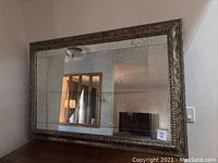 Front angle view of the large rectangular silver framed mirror showing ornate decorative details along the frame and antiquing on the glass surface.