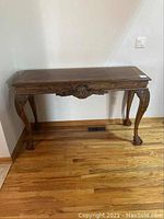 Full view of wooden console table with carved legs and apron against wall on hardwood floor.