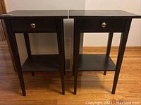 Front view of two matching dark wood night tables with drawer and lower shelf standing side by side on hardwood floor.