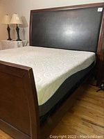 Side angle showing the king size mattress on the sleigh bedframe with the black leather headboard and wood footboard visible.