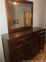 Front view of dark wood 9 drawer dresser with mirror resting on top.