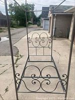 Photo of metal twin four poster bedframe outdoors showing decorative scrollwork and canopy frame from headboard view.