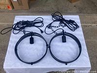 Two black metal circular pendant light frames with long black hanging cords, chains, and plugs shown on a white background.