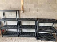 Front view of multiple black plastic shelving units with 3 tiers each showing vented grid shelves.