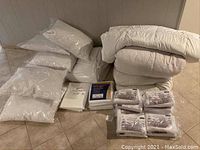 Photo showing all bedding items including duvets, pillows, duvet covers, mattress protectors, and pillow protectors packed on the floor.
