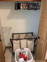 Laundry area showing 3-bin rolling hamper with beige fabric bags on black frame, white laundry basket holding detergent bottles