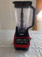 Front view of red and black Ninja blender with clear container and handle.
