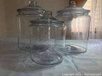 Three clear glass storage jars: two large ones and one medium sized, all with lids.