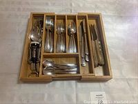 Top view of bamboo drawer organizer filled with cutlery and tools showing compartments with forks, spoons, knives, and wine opener.