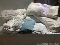 Photo showing white twin down duvets, mattress toppers and assorted bedding folded and arranged together.