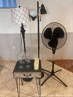 Full view of all items: fan, two floor lamps, side table, wine glasses, candles