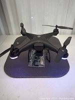 Top view of black Holystone quadcopter drone with 4 propellers, camera under front and LED lights glowing.