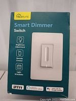 Front of retail packaging showing product name, image of the smart dimmer switch, and key features including brightness adjustment, remote control, and light schedules.
