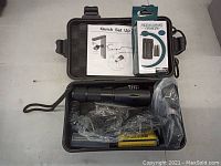 Open carrying case showing flashlight, rechargeable batteries, charger, wrist strap, and instruction manual.