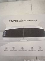 Box showing product name ST-201B Eye Massager with icons for Bluetooth, graphene heating, pneumatic kneading, vibration massage, and 180° folding features.