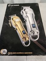 Closed packaging box featuring silver and gold clippers with digital displays, advertising cord and cordless operation.
