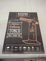 Front of box showing product name, image of torch, and use cases such as toast, smoke, ignite, melt, sear, roast, burn, solder.