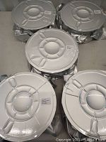 Five large spools of 3D printer filament sealed in metallic silver bags with white labels visible on top