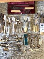 Full overview of assorted Community flatware and serving pieces laid out, several wrapped in plastic, including forks, spoons, and knives with faux ivory handles and ornate silver detailing.