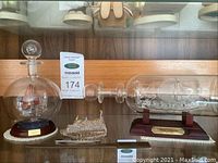 Three glass ships on display: two ships in bottles on wooden stands with plaques, one smaller standalone ship in front.