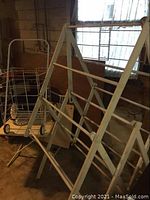 Photo of wooden folding clothes drying rack and folding metal shopping cart in basement setting
