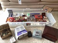 Photo of large plastic bin containing various jewelry items and several jewelry boxes and packaging placed on carpet