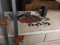 Several 5-foot metal bar clamps with orange adjustable levers and some smaller clamps, laid flat on a surface