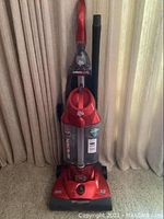 Front view of red Dirt Devil upright vacuum cleaner, showing handle and dust cup with labels.