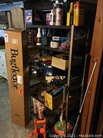 Photo of metal shelving filled with various automotive liquids, sprays, boxes, and tools, with boxed Bugflector leaning next to it.