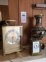 Photo showing the larger Seiko mantle clock, smaller brass mantle clock, and decorative vase on wooden surface against wood paneled wall.