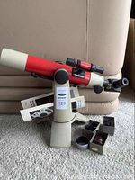 Oblique front view showing telescope tube, tripod mount, instruction manual and eyepiece boxes on carpet