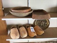 Shelf with two pairs of wooden Dutch shoes, brass plate behind, and wooden bowls above