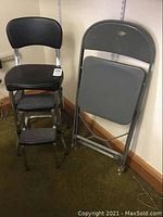 Photo of black vinyl cushioned stool with two step up footrests and gray folding chair against beige wall on green carpet.