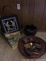 Overall lot grouping with large basket holding framed dancer artwork and brocaded cloth next to a smaller basket with wooden candle holders, brush, ceramic bowl, and bracelets.