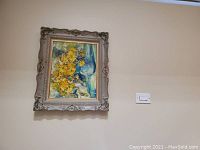 Framed painting of yellow flowers on wall, showing entire artwork and frame details.