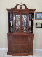 Full front view of wooden secretary desk with glass doors on top cabinet, drawers, and side doors.
