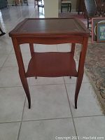 Front view of the wooden end table standing on tile floor with a lower shelf and curved legs