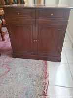 Front view of wood cabinet with two upper drawers and two-door lower storage with round metal knob pulls, medium brown finish.